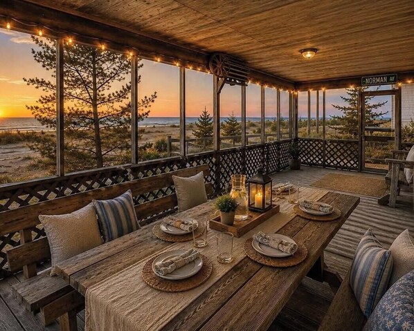 Um deck de madeira com mesa posta para refeições, com vista para a praia e o oceano.