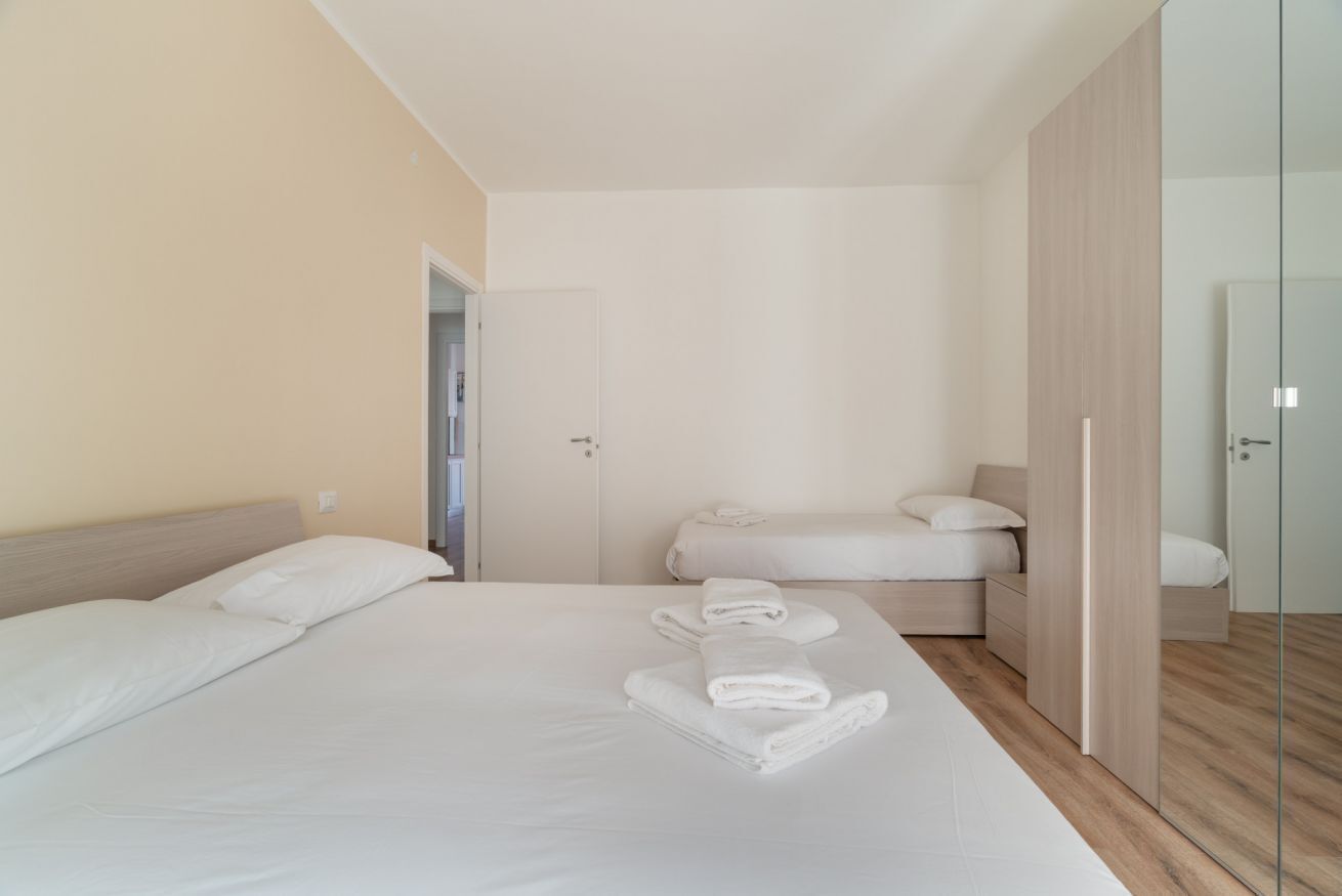 A modern hotel room with a large bed, a smaller bed, a wardrobe, and a door leading to another room.