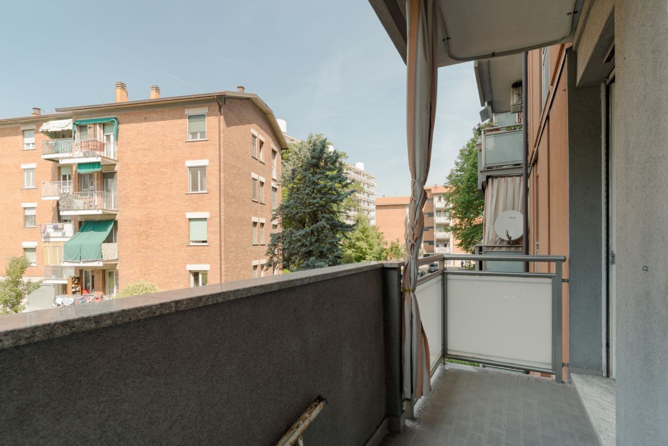 Ein Balkon mit Blick auf benachbarte Gebäude, einem Metallgeländer und einer Tür zu einem Innenraum.