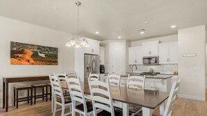 Een moderne keuken met witte kasten, een centraal eiland en een eethoek met witte stoelen.