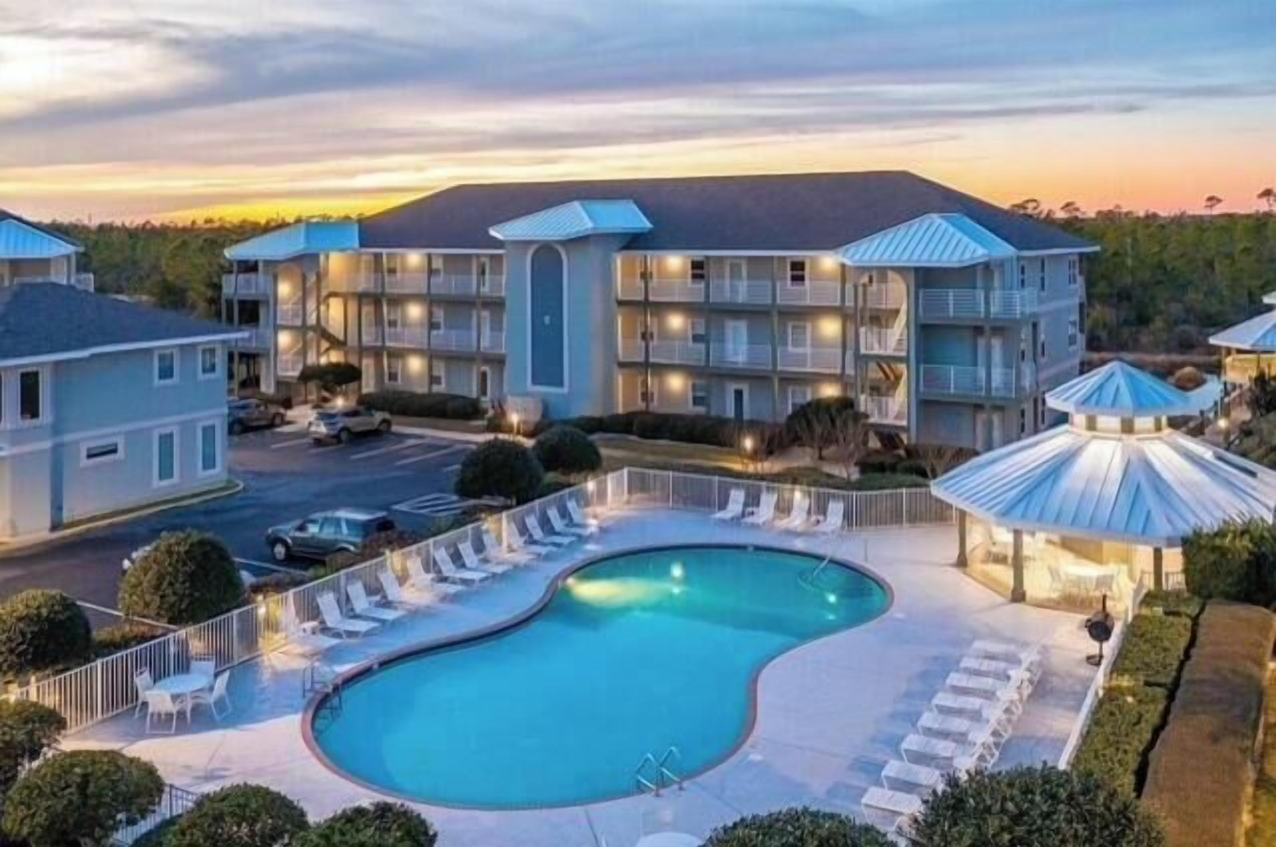 A hotel with a swimming pool, multiple balconies, and a parking area.