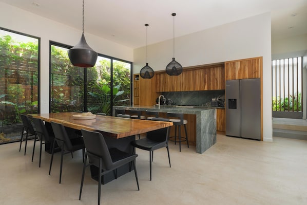 Una cocina moderna con una mesa de comedor de madera, sillas negras y lámparas colgantes.