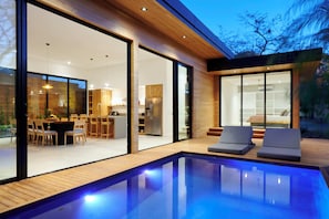 Una casa moderna con piscina, grandes puertas de vidrio y un comedor.