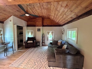 Un accogliente soggiorno con soffitto in legno, un divano verde, una poltrona marrone e un tappeto decorato.