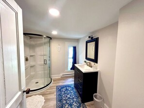 Un bagno con box doccia in vetro, un lavabo con mobile scuro e un tappeto azzurro a motivi decorativi.