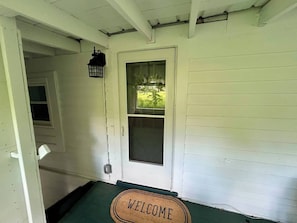 Una porta bianca con una finestra, un tappetino d'ingresso e una lanterna sul portico.