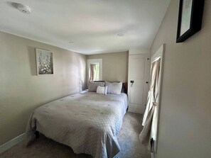 Ein Schlafzimmer mit Bett, Fenster, Tür und einem gerahmten Bild an der Wand.