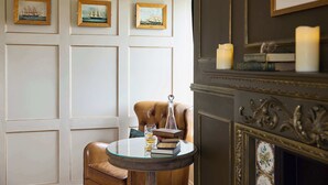 A room with a leather armchair, a round table with books and a glass, and framed pictures on the wall. - Host & Stay | The Chimneys, Whitby (Whitby)
