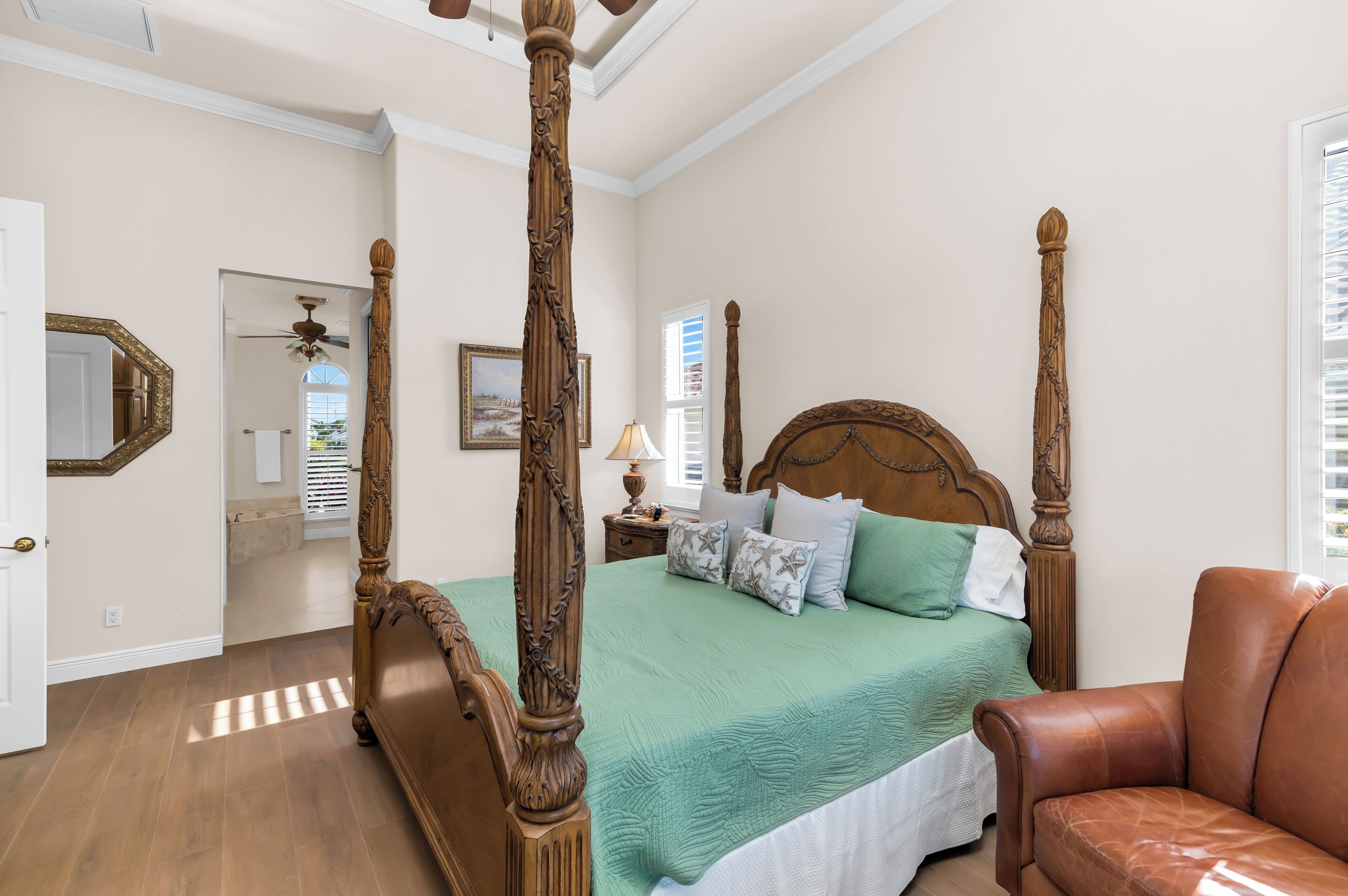 Un lit à baldaquin avec une couvre-lit verte, un fauteuil en cuir marron et une tête de lit en bois.