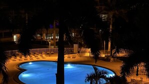 Vista nocturna d'una zona de piscina d'hotel amb una piscina circular, gandules i palmeres.