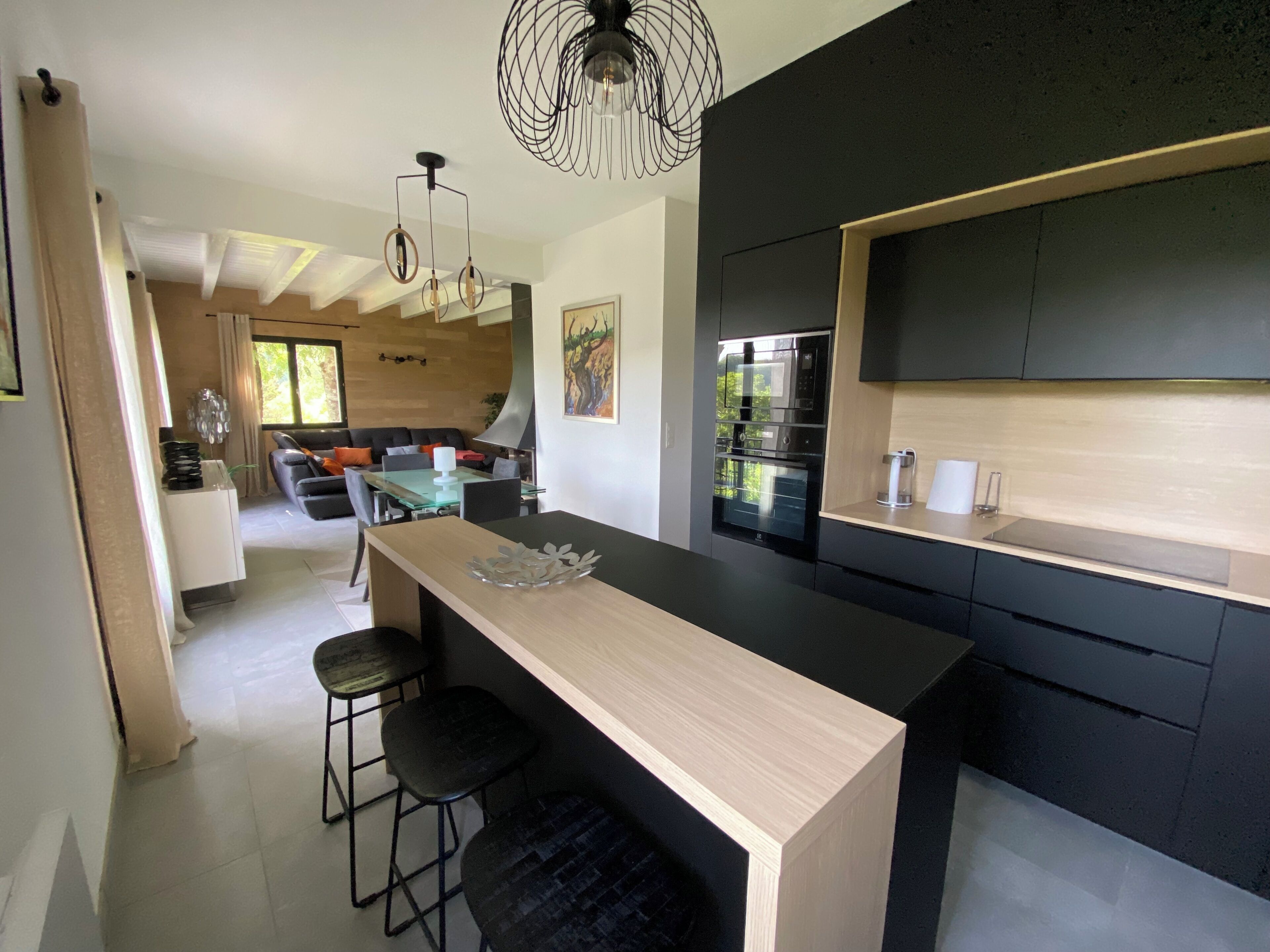 Een moderne keuken met een centraal eiland, zwarte kastjes en een eethoek met een glazen tafel en stoelen.