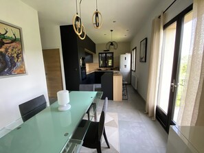 A modern kitchen with a central island, a dining area with a glass table, and a large window with curtains. - Contemporary home with a view of the mountains (Pont de Montvert - Sud Mont Lozère)