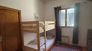 Ein Zimmer mit einem Etagenbett, einem Kleiderschrank, einem Heizkörper und einem Fenster mit Vorhängen.