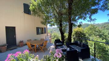 Une terrasse avec une table et des chaises, un canapé et une vue sur une colline.