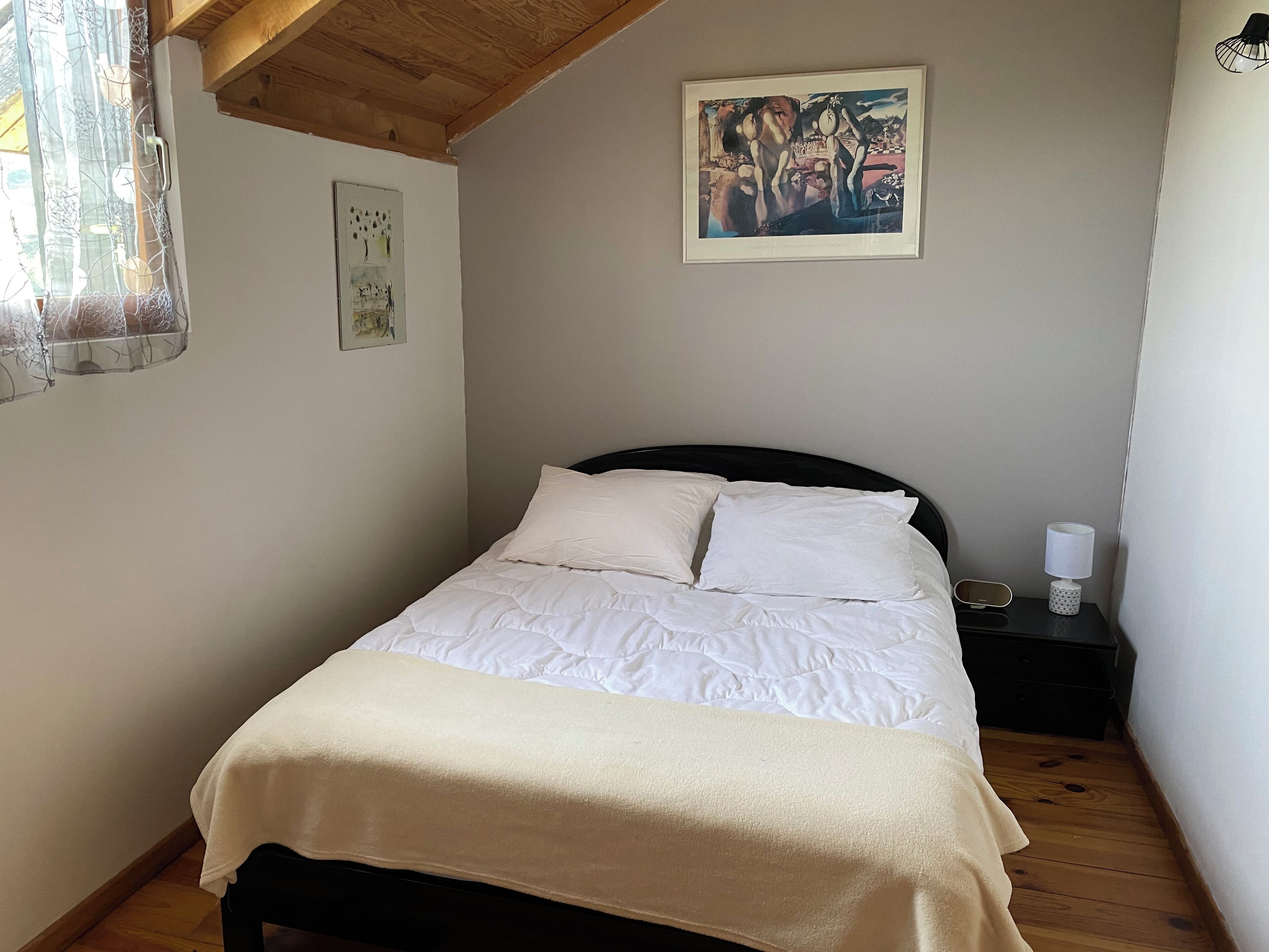 A bedroom with a bed, a nightstand, a lamp, and two framed artworks on the wall.