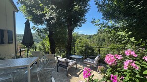 Un patio al aire libre con asientos y una mesa, rodeado de árboles y flores.