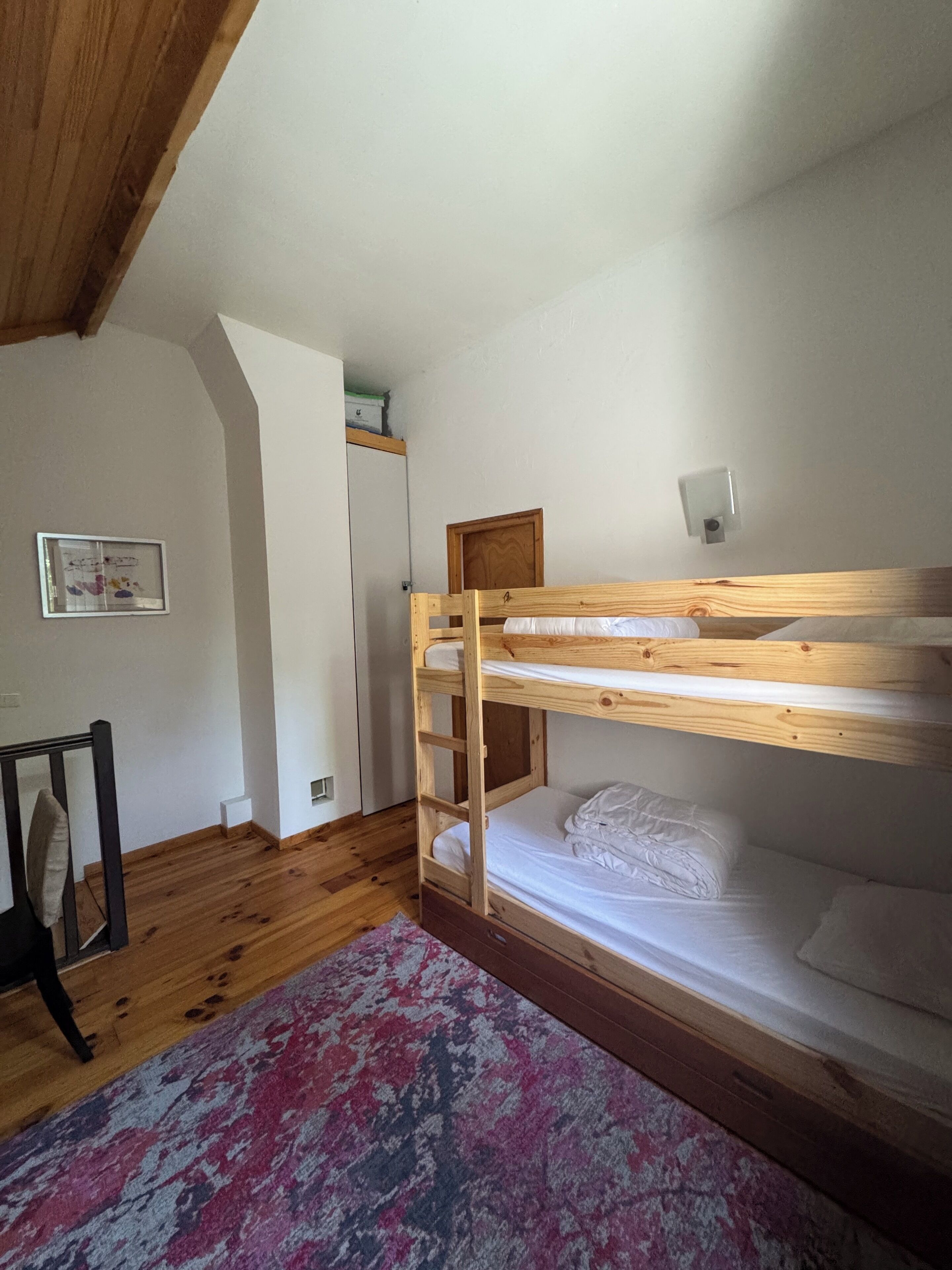 Une chambre avec un lit superposé, une tête de lit en bois, une petite table de chevet et un tapis à motifs.