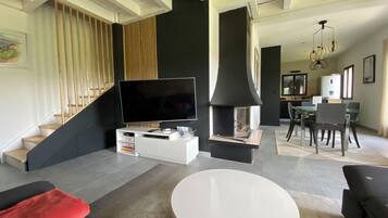 Un salon moderne doté d’un téléviseur à écran plat, d’une cheminée, d’un coin repas et d’un escalier.