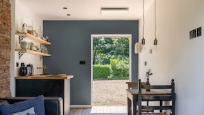 Un interior moderno con una pared gris oscuro, estantes de madera, un sofá de cuero negro, una mesa de comedor con sillas y vistas a un sendero de grava que conduce a un área verde.