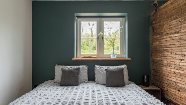 Un dormitorio con cama, dos almohadas, ventana con vistas y pared de madera.
