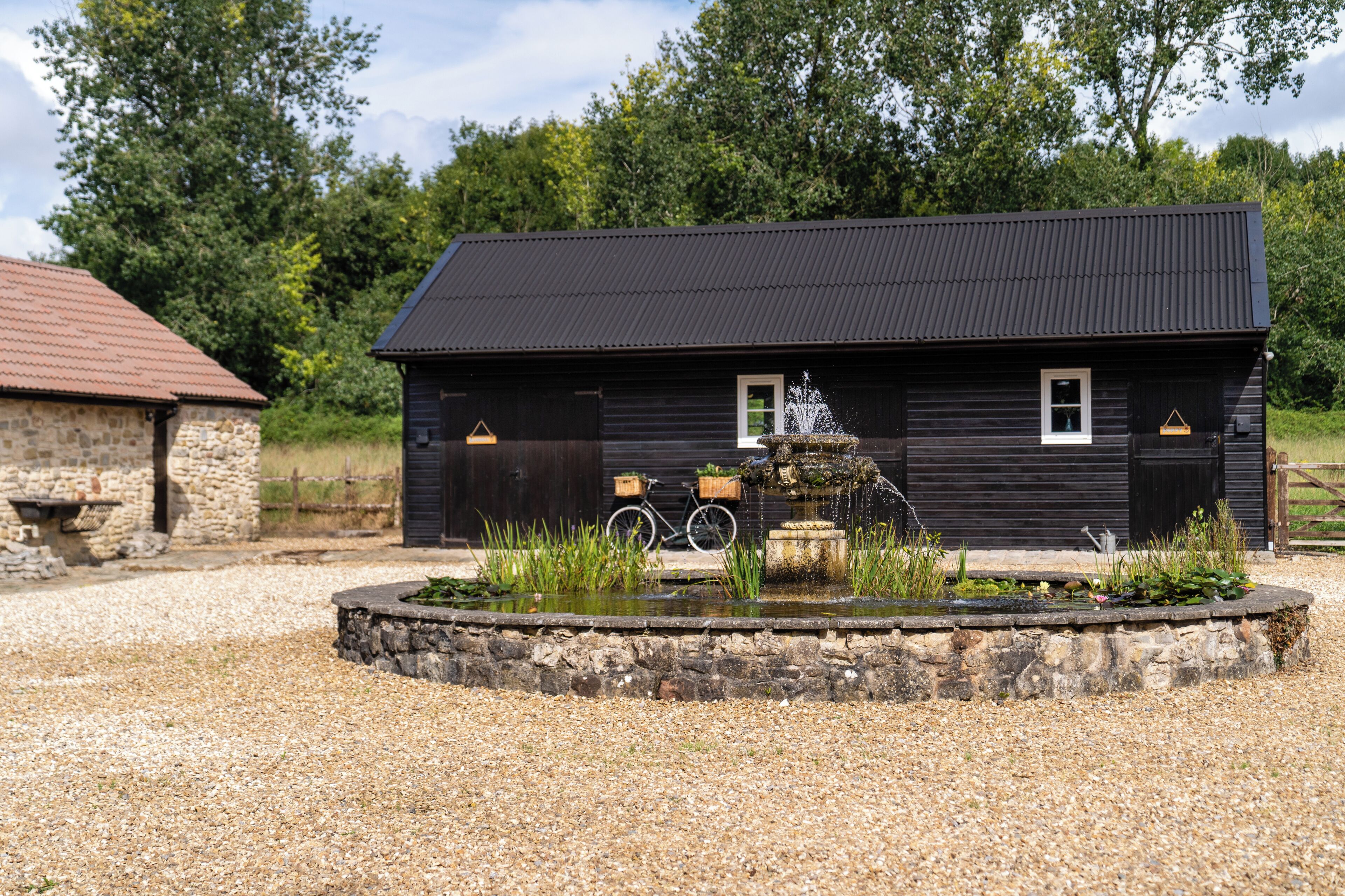 A rustic building with a metal roof, a stone wall, and a small pond with a fountain.