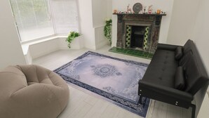 A living room with a fireplace, a beige sofa, a black sofa, and a patterned rug. - 5 Gelli Terrace (Caerphilly)
