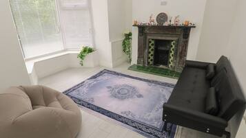 A living room with a fireplace, a beige sofa, a black sofa, and a patterned rug.