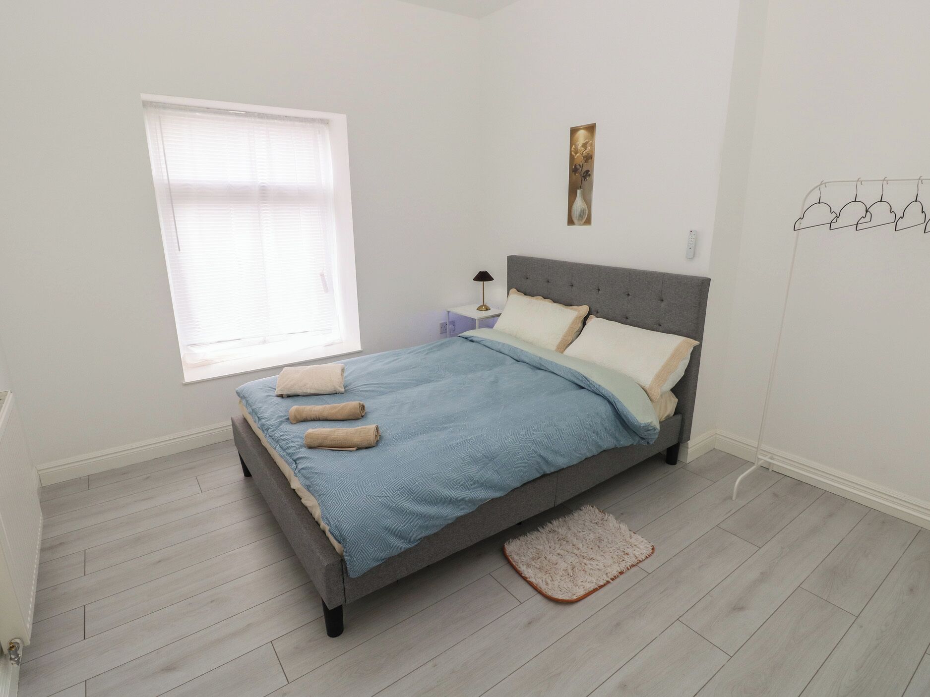 A bedroom with a bed, a window, a bedside table, a lamp, and a wall-mounted light fixture.