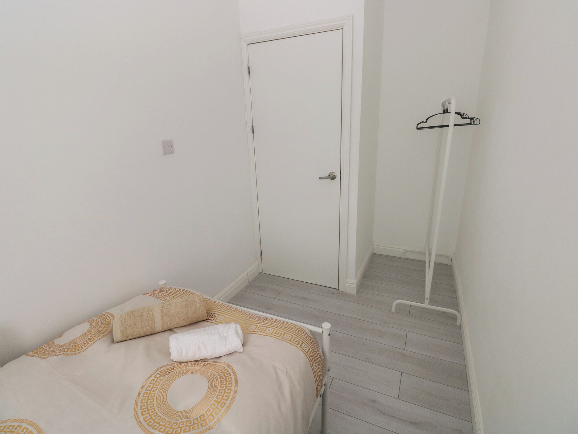 Een kleine, schone kamer met een bed, een witte deur en een kapstok.