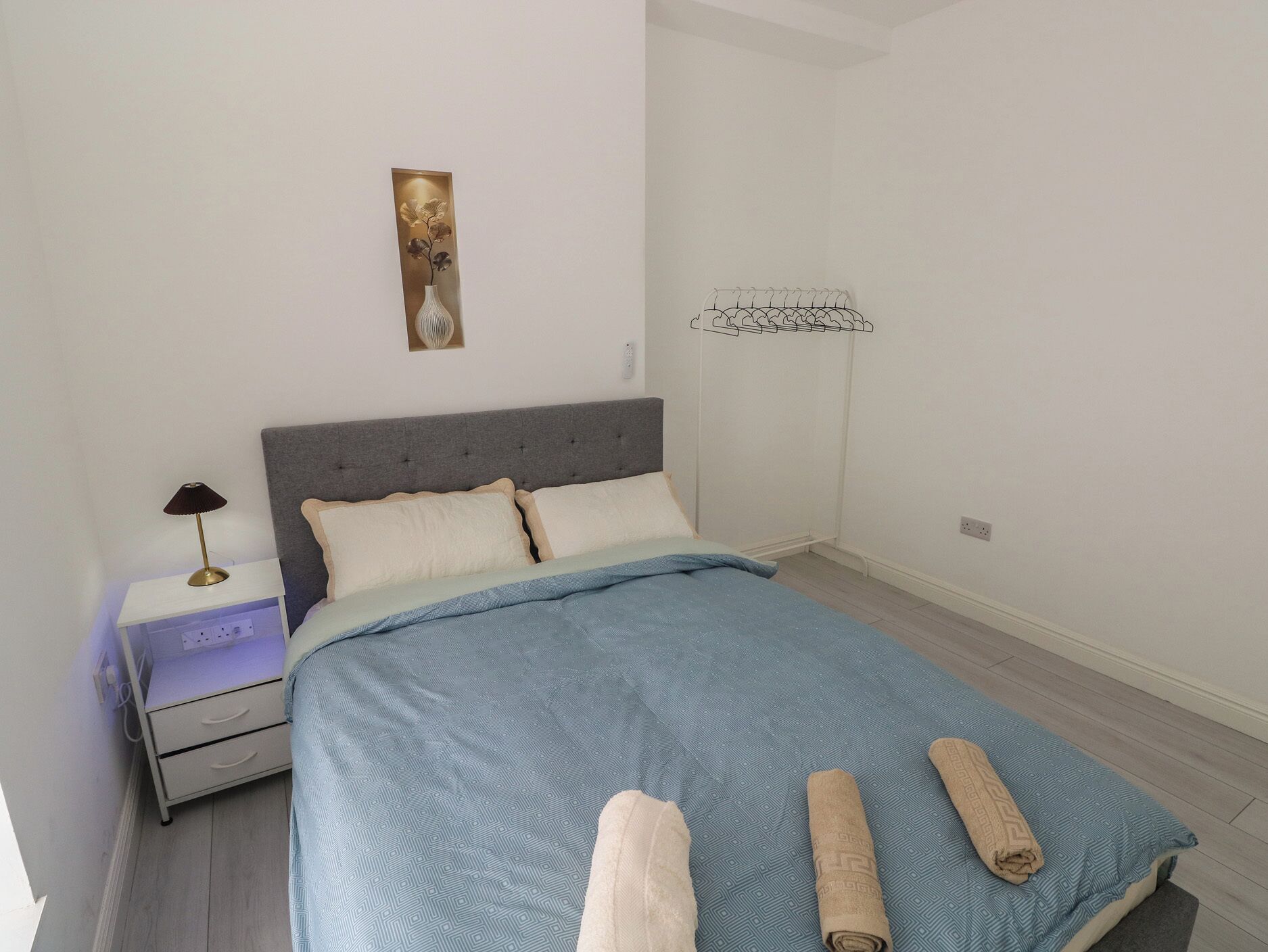 Une chambre à coucher comprenant un lit, une table de chevet, une lampe fixée au mur et un élément décoratif placé au-dessus du lit.