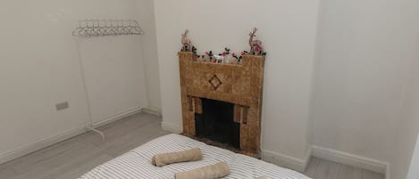 Un dormitorio con cama, chimenea, perchero y toma de corriente.