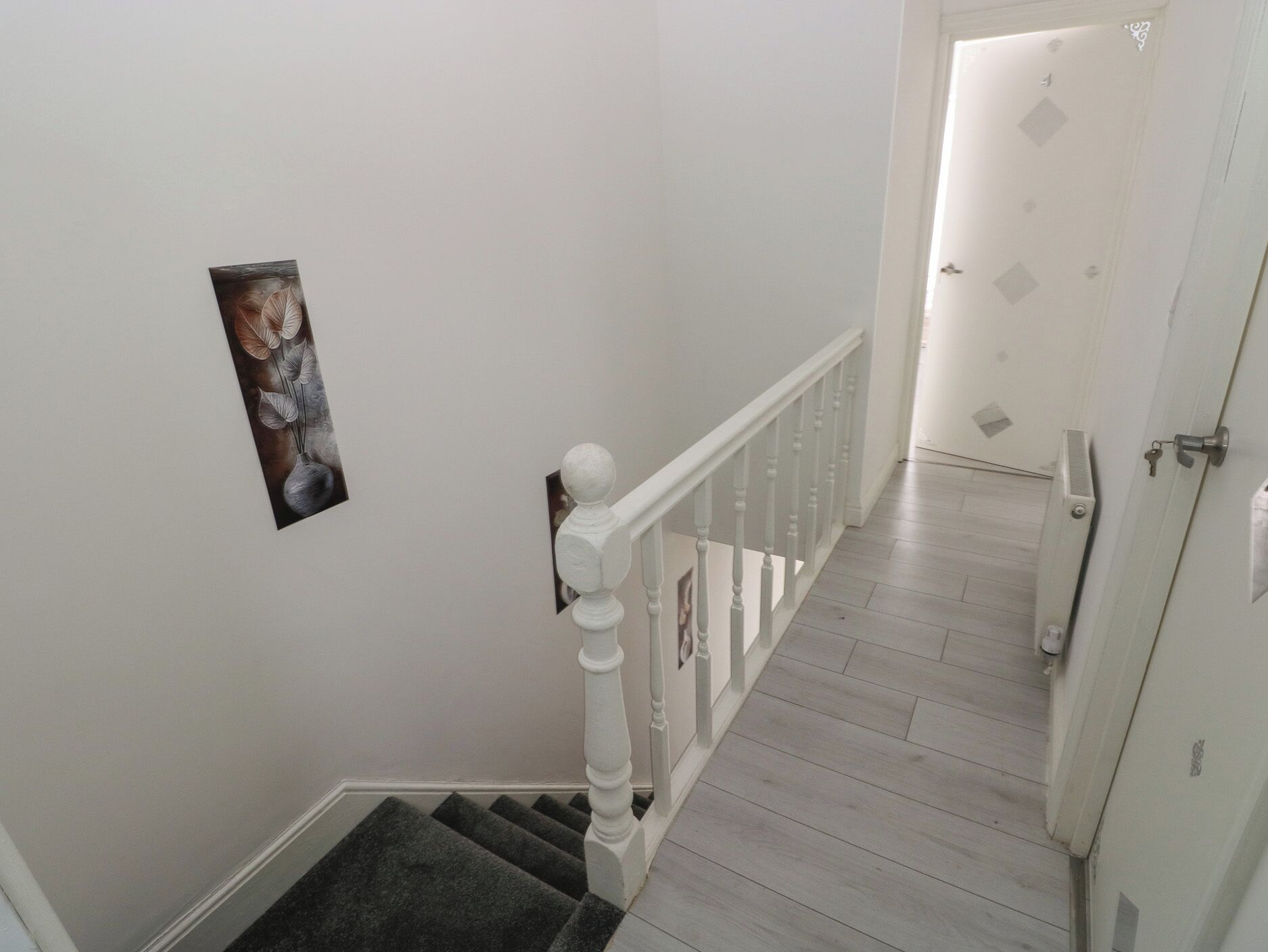 A staircase with a white railing, a door with a keyhole, and a framed picture on the wall.