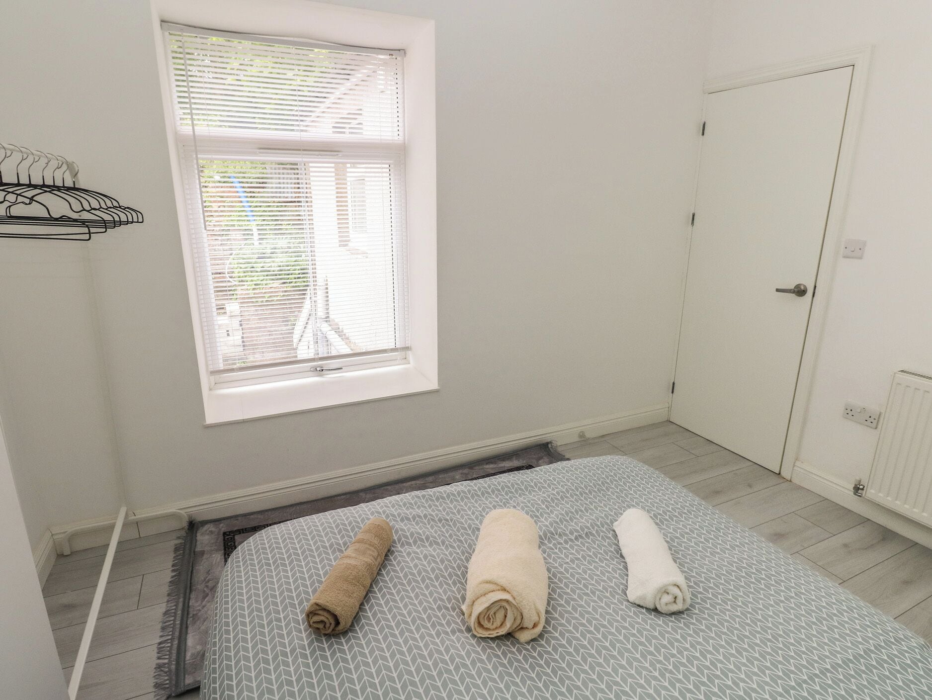 A room with a bed, a window with blinds, a door, and a radiator.
