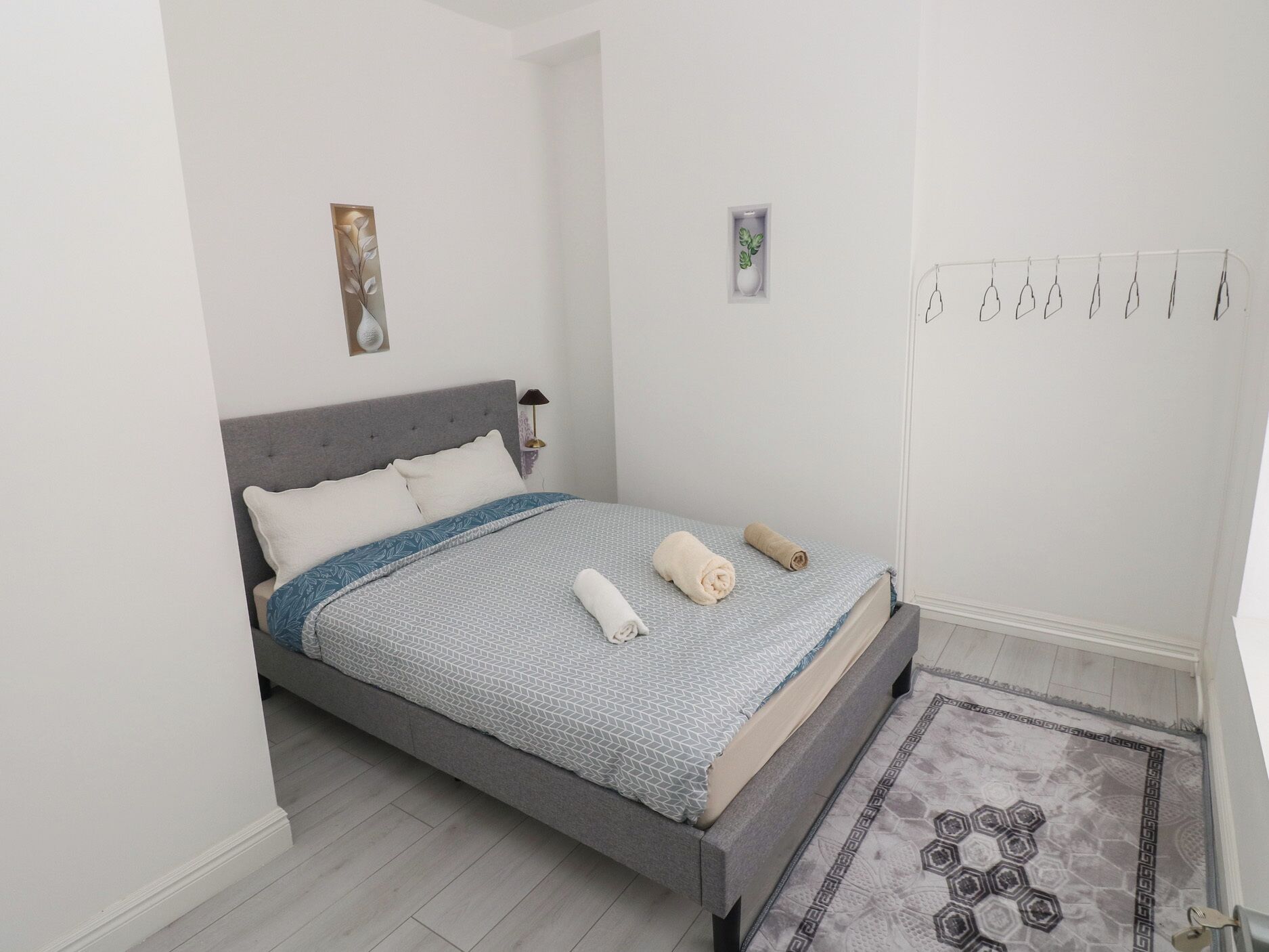 Un dormitorio con cama, mesita de noche, lámpara de pared y una pequeña planta en maceta.