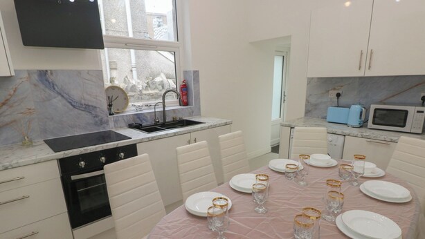 A modern kitchen with white cabinets, a marble backsplash, a dining table set for six with white plates and glasses, and a microwave. - 5 Gelli Terrace (Caerphilly)