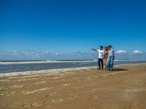 A beach with footprints leading to the water, a clear sky, and a person pointing. - Comfort Connecting Room 2 (Velsen-Zuid)