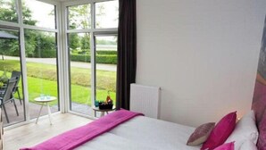 Ein Schlafzimmer mit einem großen Bett, Blick ins Freie und einem kleinen Tisch mit Getränken.