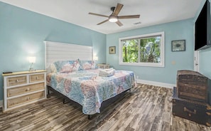 A bedroom with a bed, a ceiling fan, a window with a view, and a dresser. - Charming 3 Bedroom Cottage, Guest Cards + Cart! (Fripp Island)