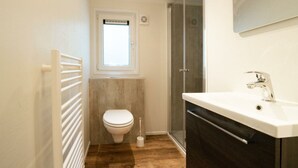 A bathroom with a toilet, a window, a shower, and a sink.