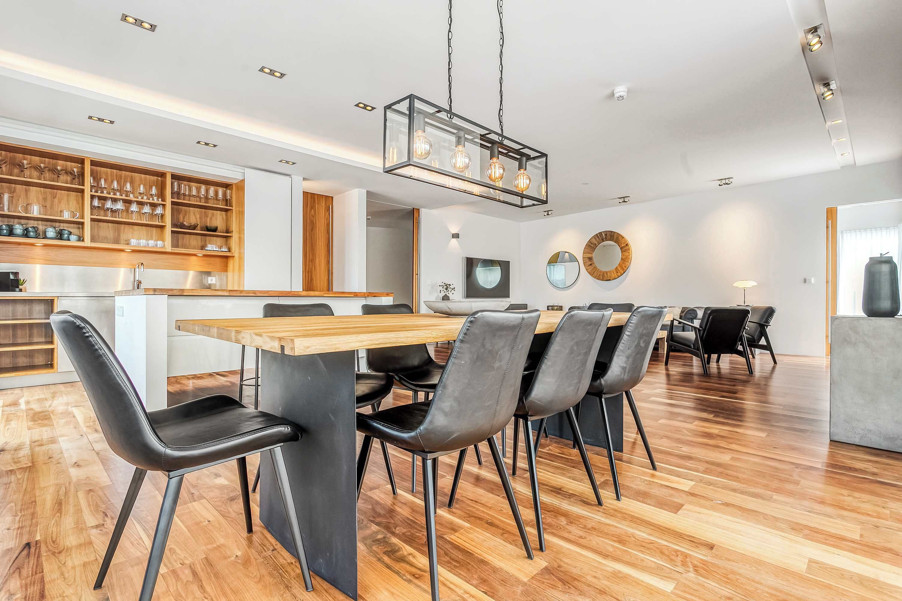 A modern dining area with a wooden table, black chairs, and a hanging light fixture.