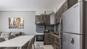 A modern kitchen with a stainless steel refrigerator, a built-in oven, and a gas stove. There is a dining table with chairs and a sofa in the adjacent living area. - Relax by the Sea | 1BR Apartment by PikHost (Durrës)