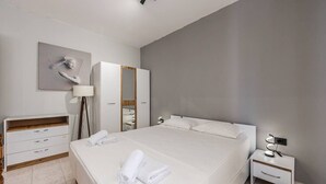 A modern bedroom with a large bed, a bedside table, a wardrobe, and a lamp. - Relax by the Sea | 1BR Apartment by PikHost (Durrës)
