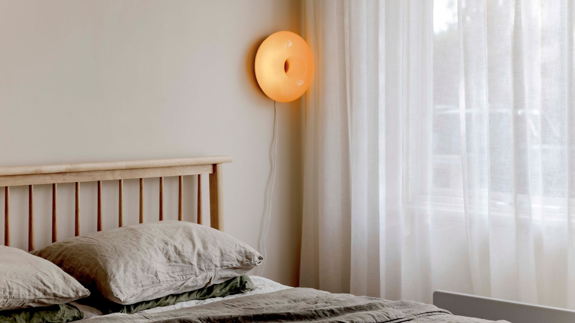 A bedroom with a wooden headboard, a bed with a green and white patterned bedspread, and a wall-mounted light fixture.