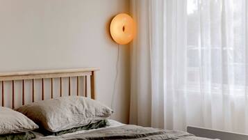 A bedroom with a wooden headboard, a bed with a green and white patterned bedspread, and a wall-mounted light fixture.
