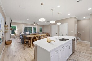 Eine moderne Küche mit Kochinsel, Pendelleuchten und einem Essbereich mit Holztisch und Stühlen.