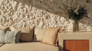 A beige sofa with pillows, a wooden cabinet, and a vase with flowers against a textured wall. - Sundara, Exclusive Seaview Estate with Grand Pool & Direct Beach Access (Σκάλα)