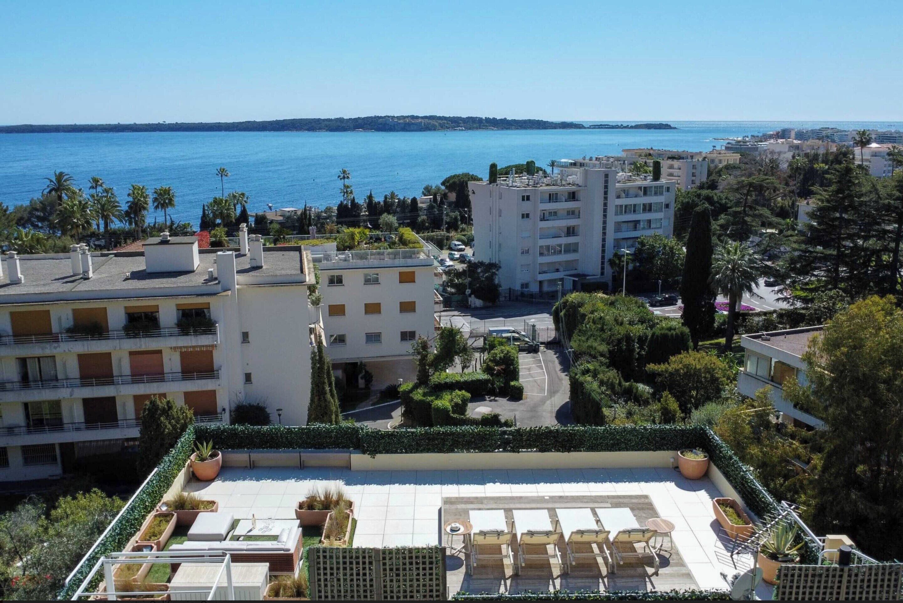 A rooftop terrace with outdoor seating, a view of the sea, and surrounding buildings.