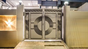Ein moderner Gebäudeeingang mit einem geometrisch gemusterten Tor, einer Steinsäule links und einer Betonwand rechts.