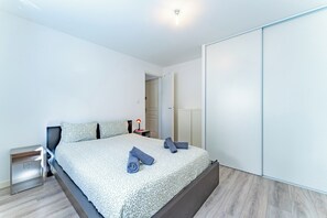 Quarto moderno com cama, mesas de cabeceira, guarda-roupa e uma porta que dá para outro espaço.