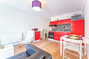 Uma cozinha moderna com armários vermelhos, uma mesa de jantar branca e um sofá preto numa sala de estar.